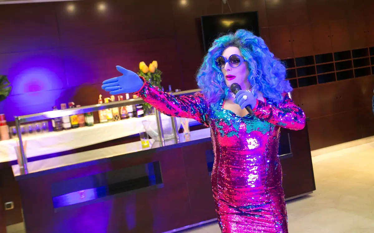 Drag queen con peluca azul y vestido de lentejuelas actuando en una cena baile